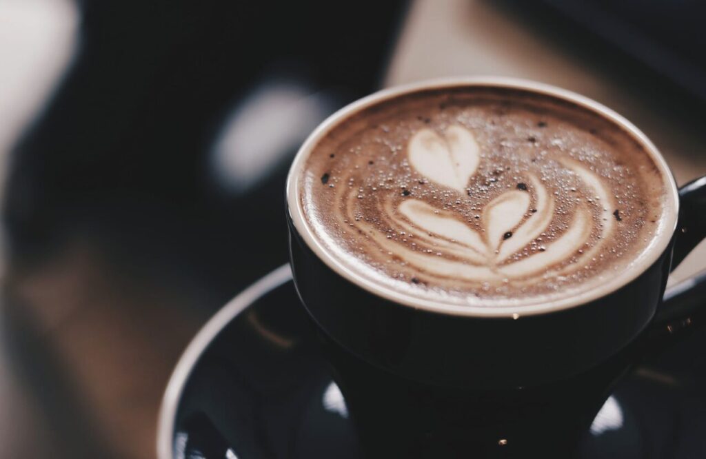 Close-up of a dark coffee cup with heart-shaped latte art on the foam surface on a saucer