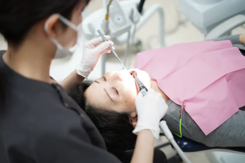 Dentist wearing mask and gloves performing a dental procedure on a patient lying in a chair.