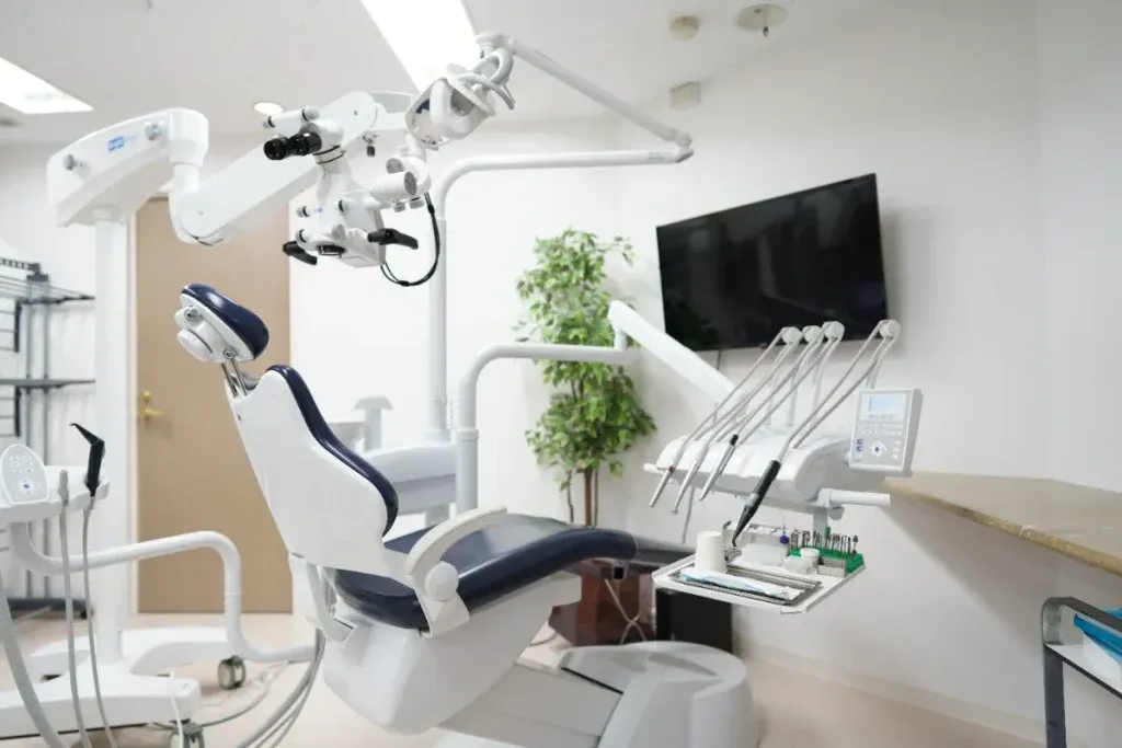 Modern dental treatment room with a reclining chair, overhead light, and multiple dental instruments ready for use in front of a wall-mounted monitor.